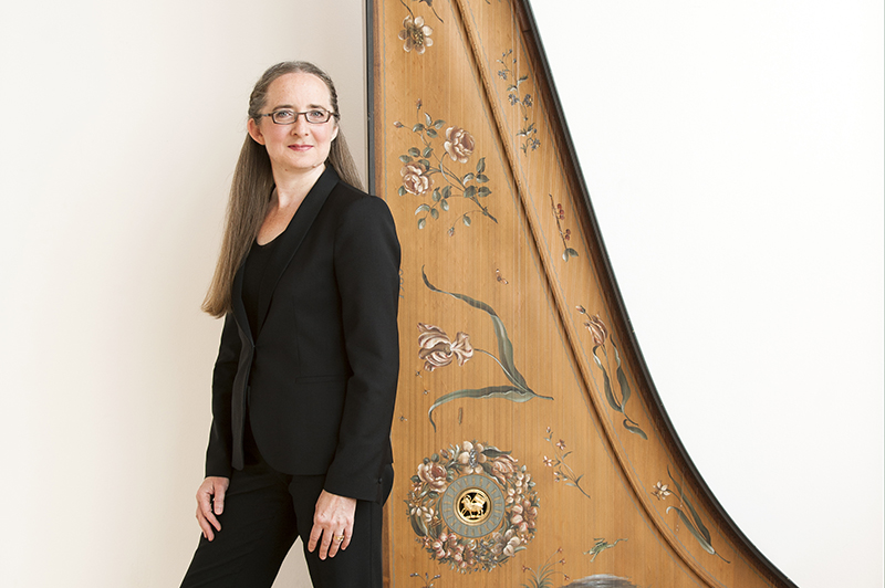 Charlotte Nediger standing in a white room next to a harpsichord standing up-right.