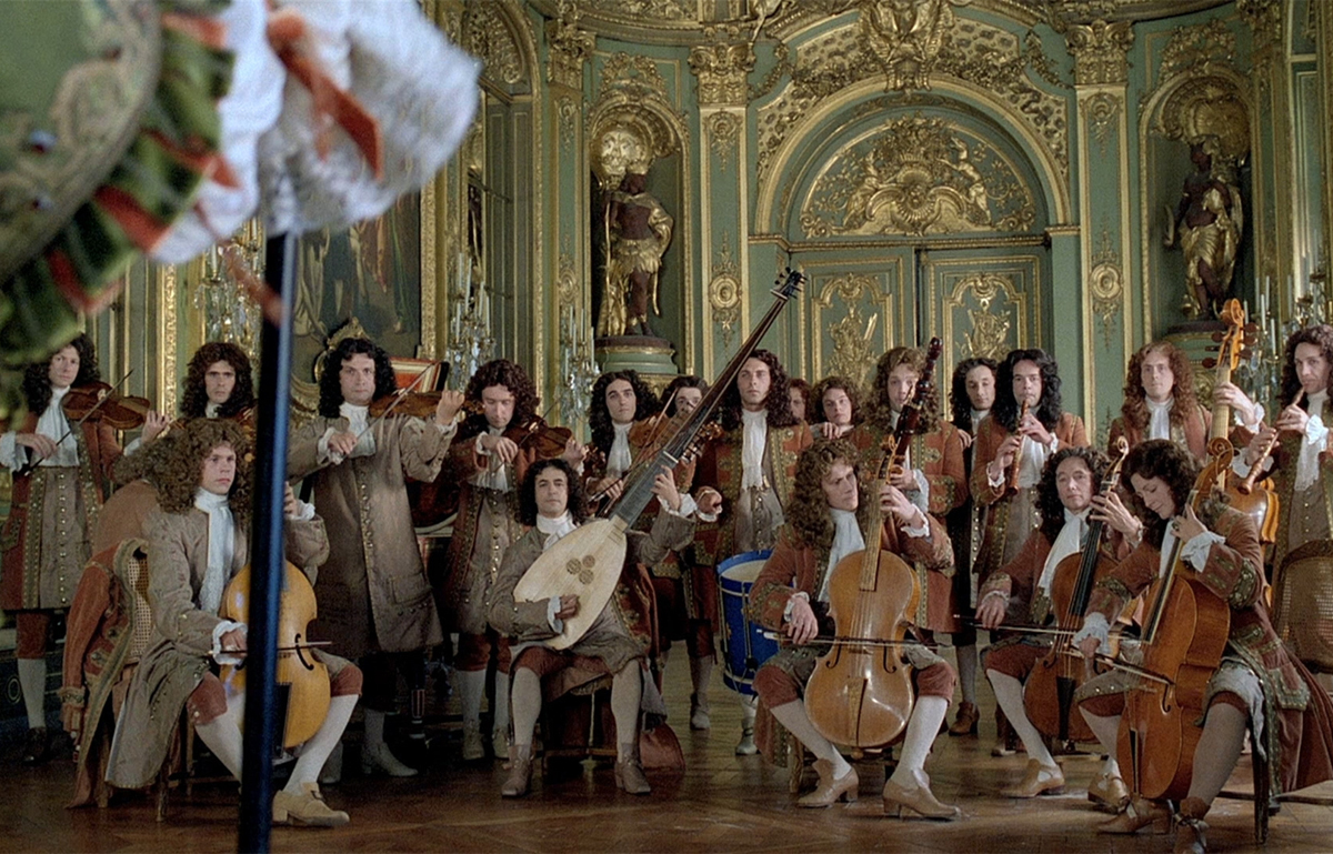 A still image from the film Tour les Matins du Monde. A large period ensemble in period clothes are packed tightly together and performing inside the Versailles palace