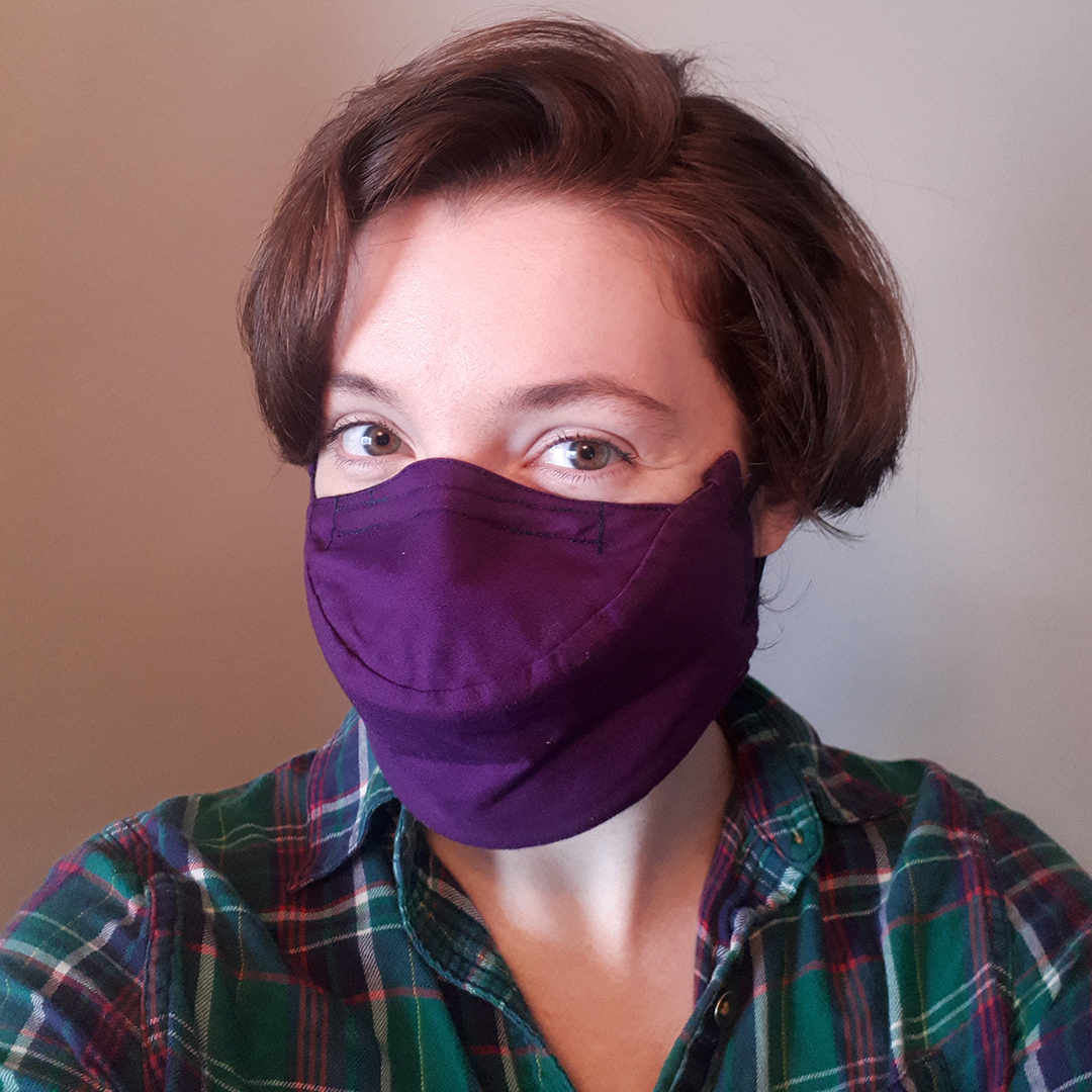 Katy Clark, a Caucasian woman with brown hair, looking directly at the camera while wearing a purple mask for vocalists