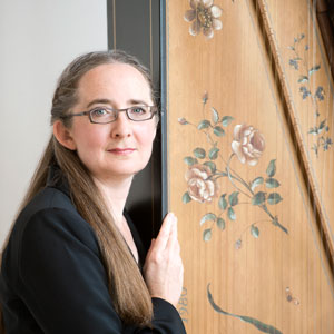 Charlotte Nediger standing next to a harpsichord standing upright. Photo by Sian Richards.