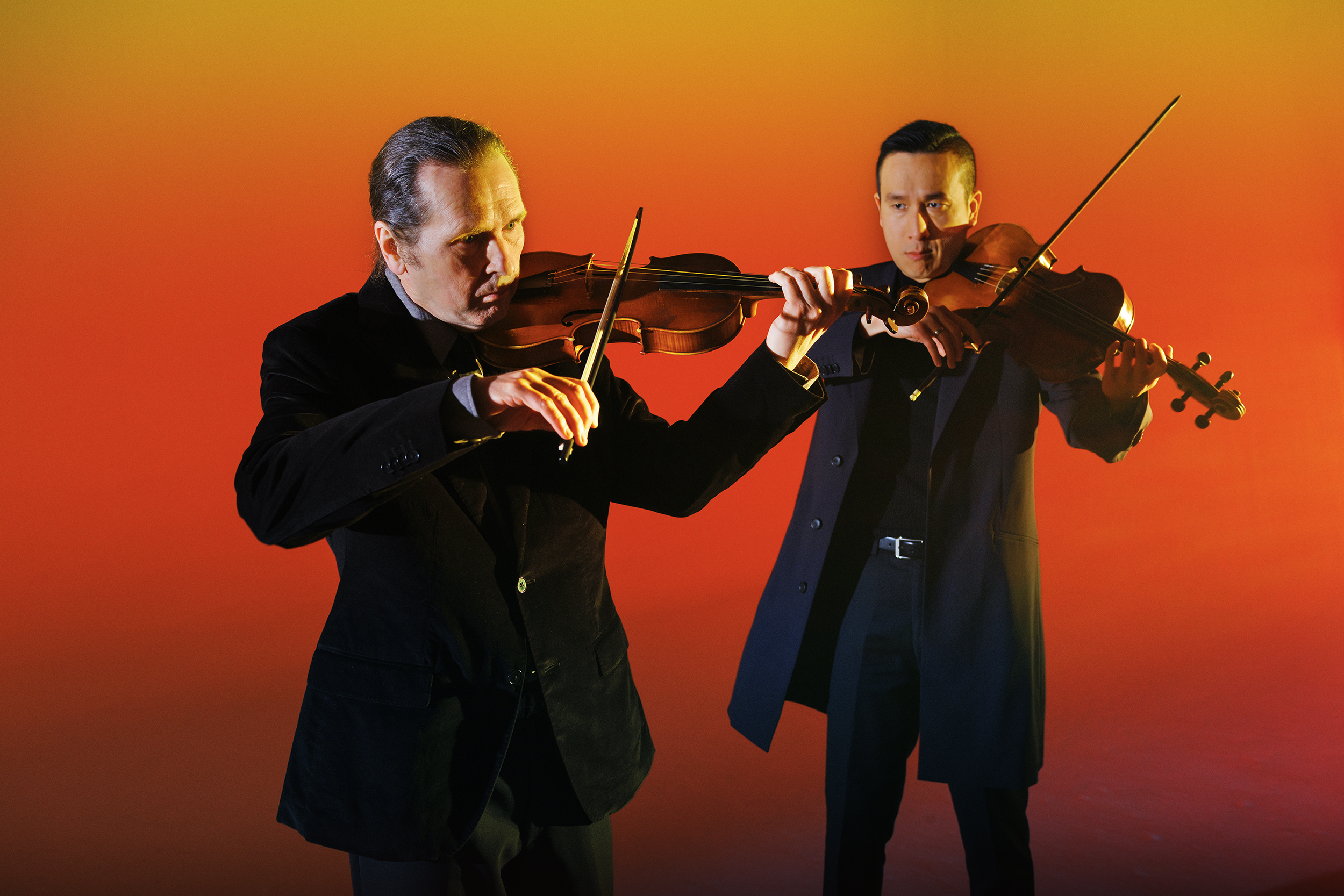 A violist and violinist posing with their instruments in a studio with a warm glow