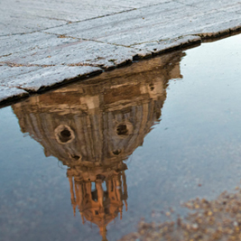 Reflection of a building's dome in a puddle of water beside the road