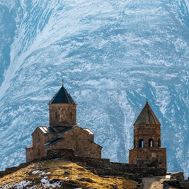 Image of a Georgian church set against blue and white mountains 