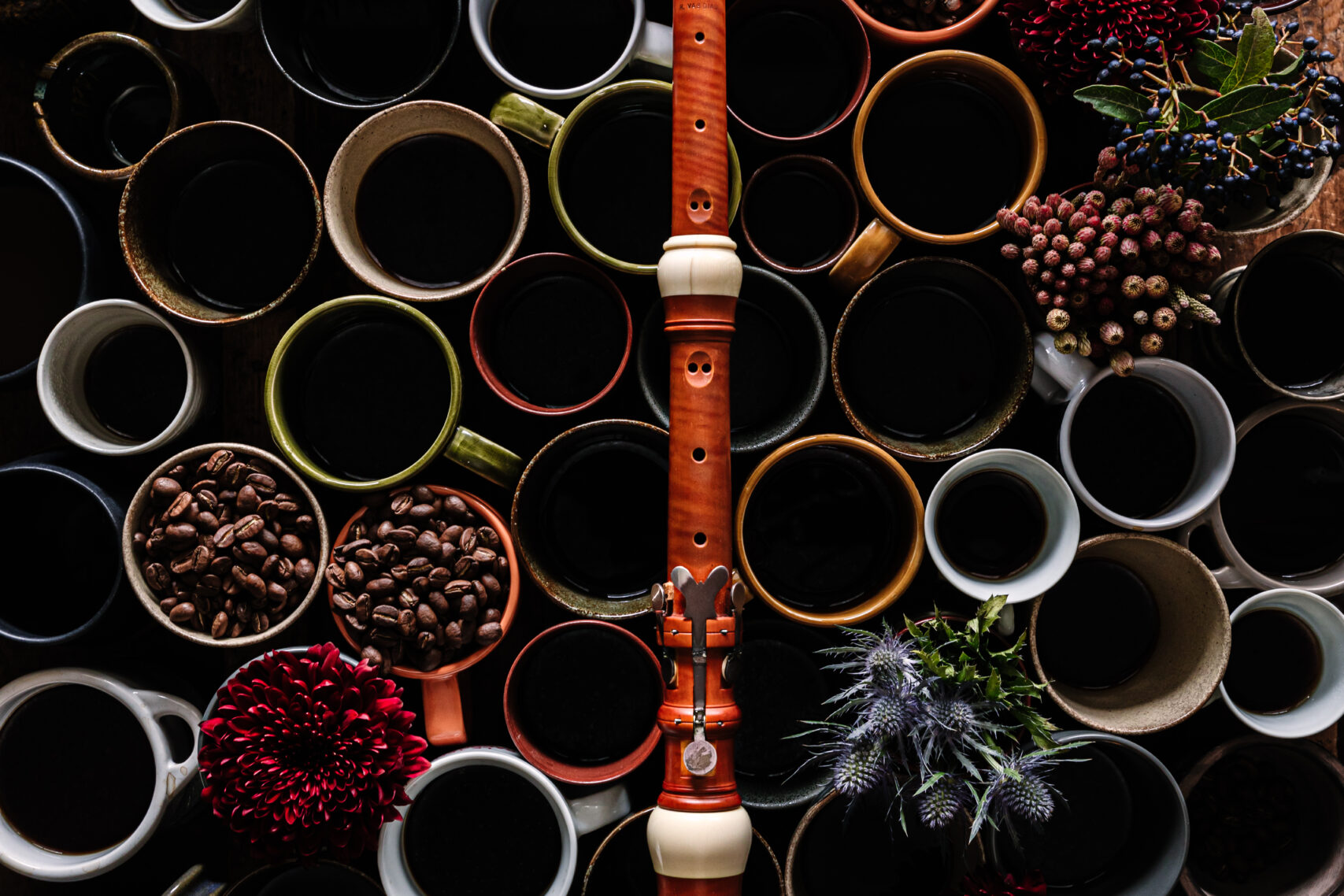 An image of random colourful mugs with a few of them filled with coffee beans and a bassoon placed on them vertically