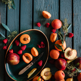 A picture of whole and halves of peaches, apricots and apples on the table with a knife