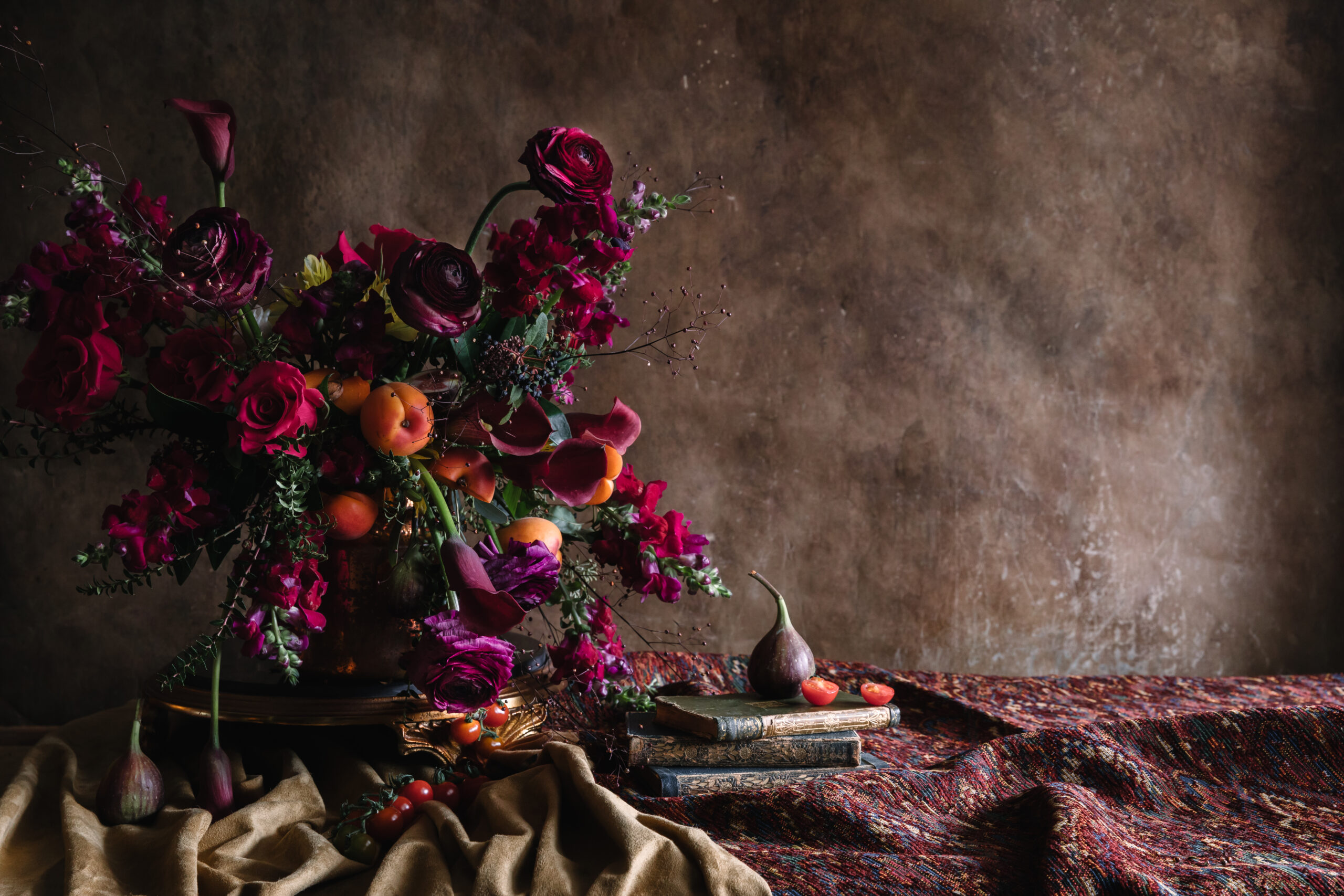 Bouquet of flowers with a fig and a half cut tomato on a pile of books.