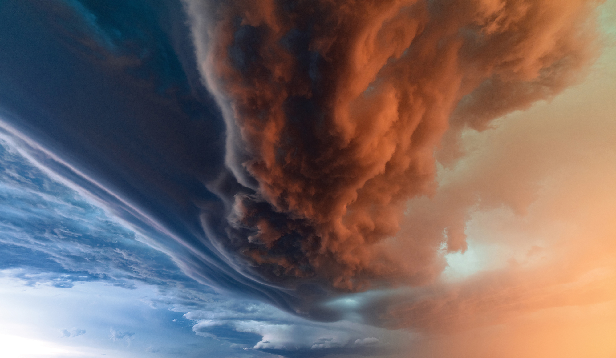 The setting sun illuminates a swirling red storm cloud against a blue and yellow sky.