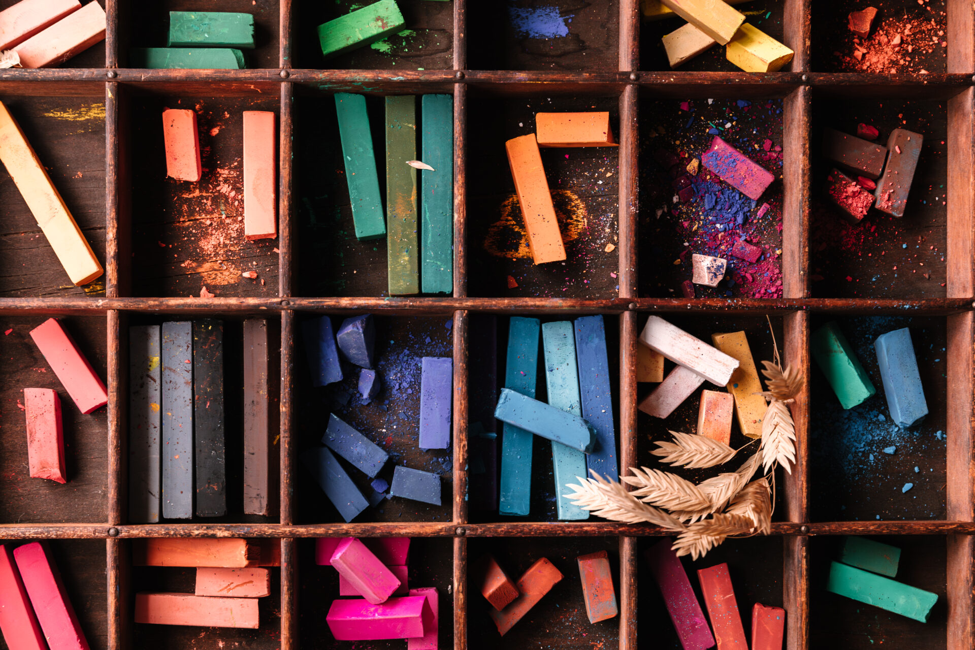 Various pieces of chalk pastel organized by colour within sections of a wooden box.