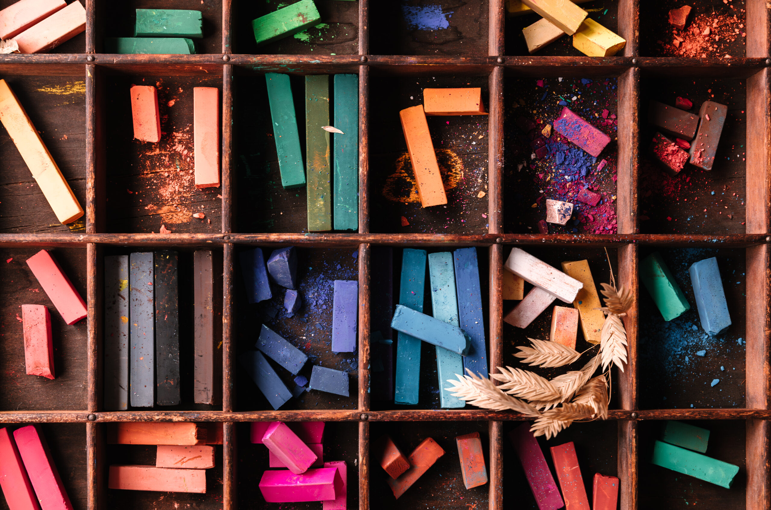 Various pieces of chalk pastel organized by colour within sections of a wooden box.