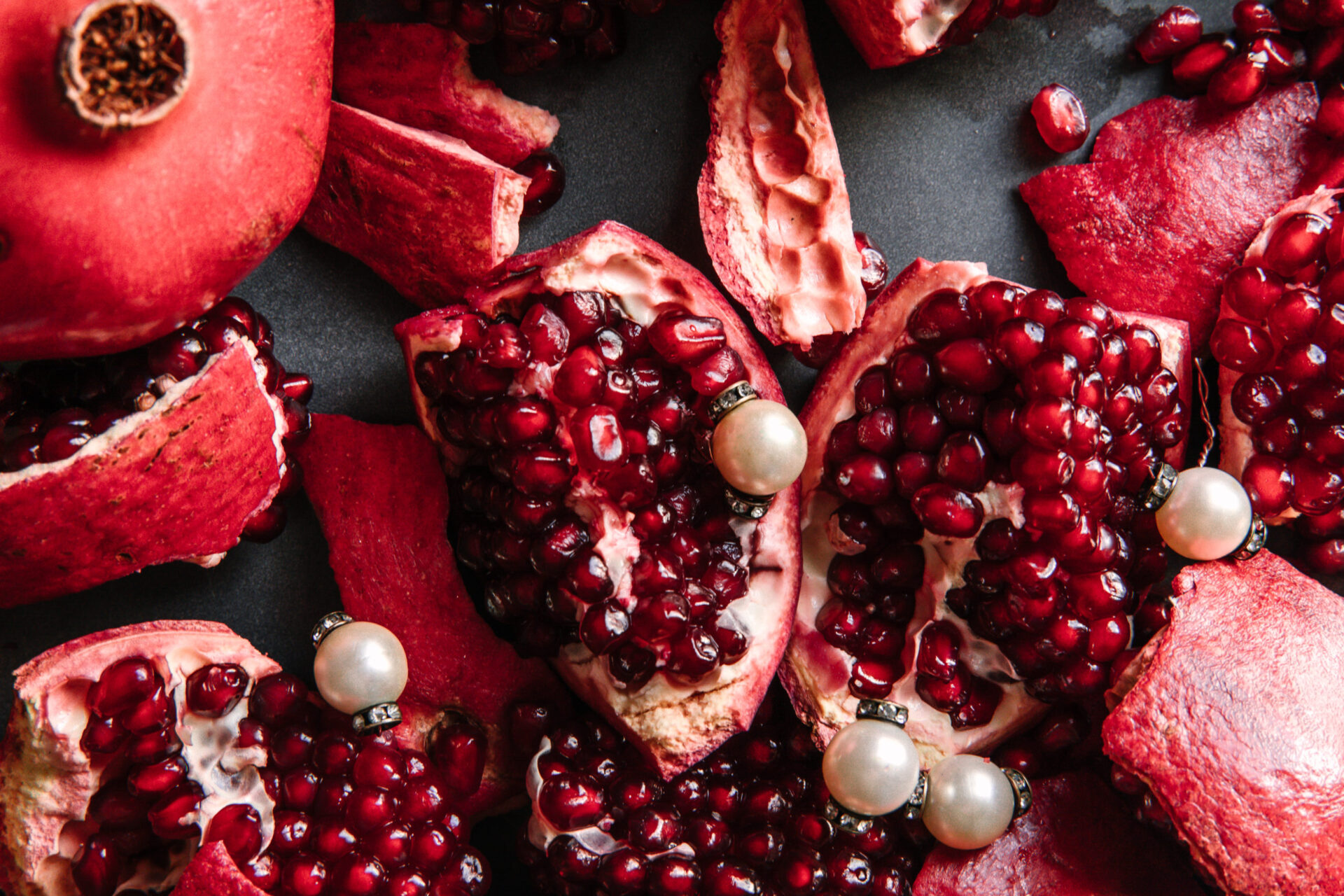 Half peeled pomegranates sit on a grey background. Three white pearls rest on the fruit.