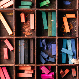 Various pieces of chalk pastel organized by colour within sections of a wooden box.