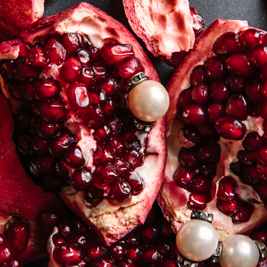 Half peeled pomegranates sit on a grey background. Three white pearls rest on the fruit.