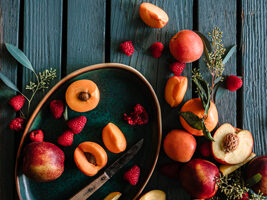 A picture of whole and halves of peaches, apricots and apples on the table with a knife