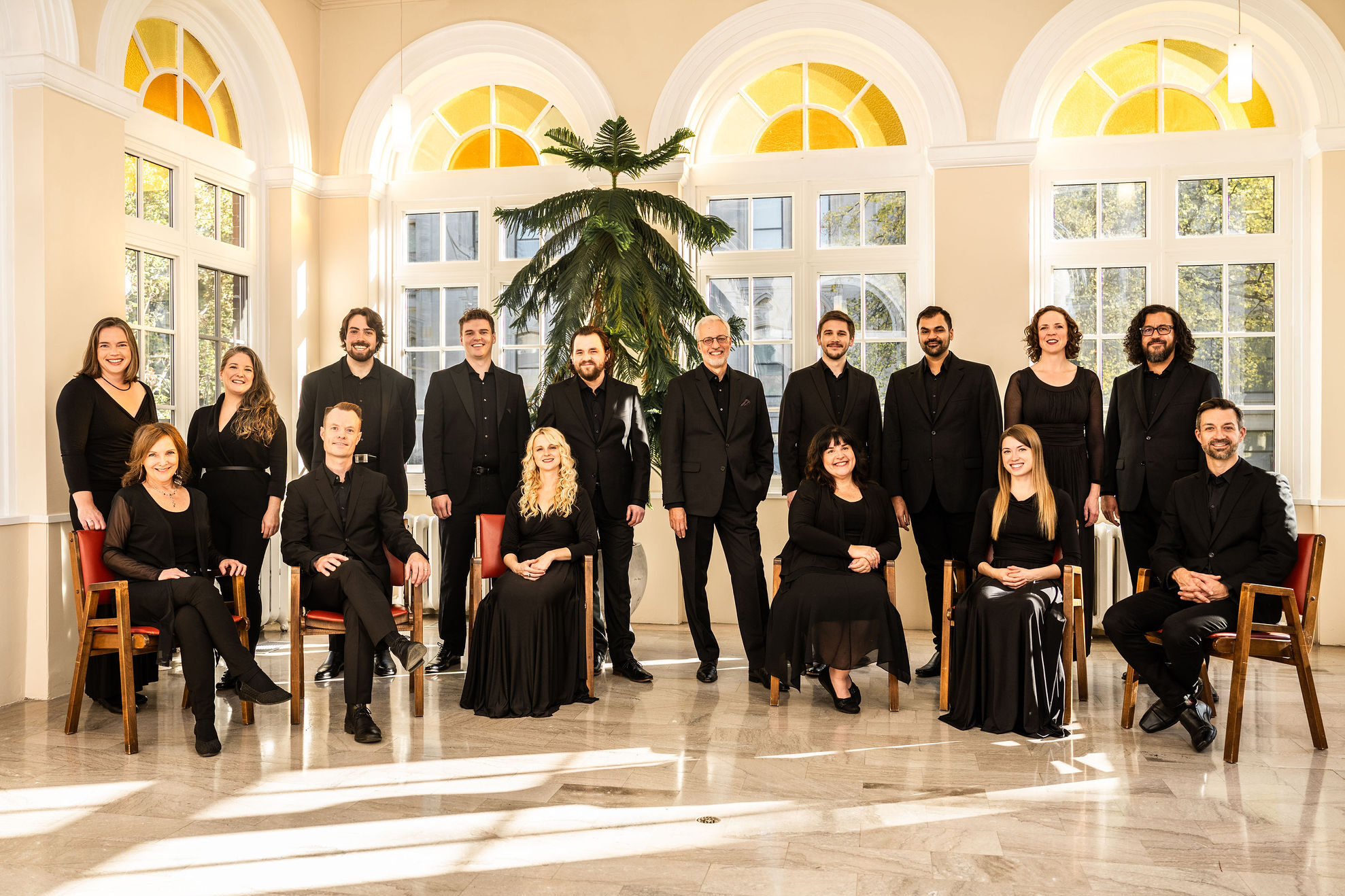 The Tafelmusik Chamber Choir in a bright and sunny room, with a tree behind them